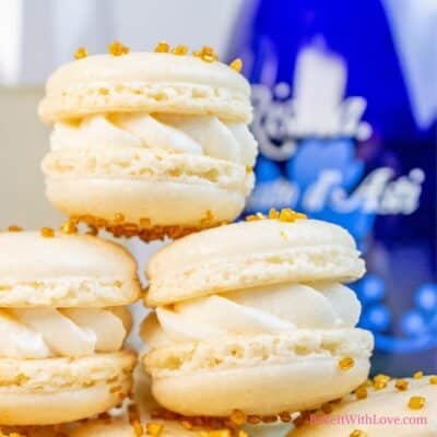 Delightfully extravagant champagne macarons stacked on a plate with a blue bottle and champagne flute in the background.