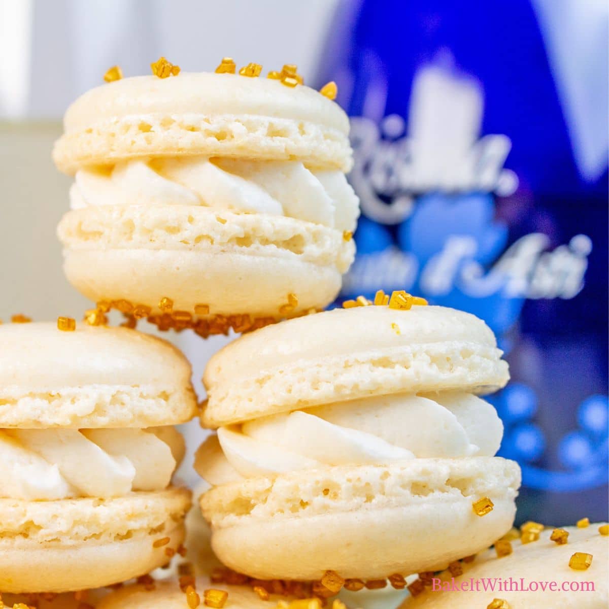 Delightfully extravagant champagne macarons stacked on a plate with a blue bottle and champagne flute in the background.