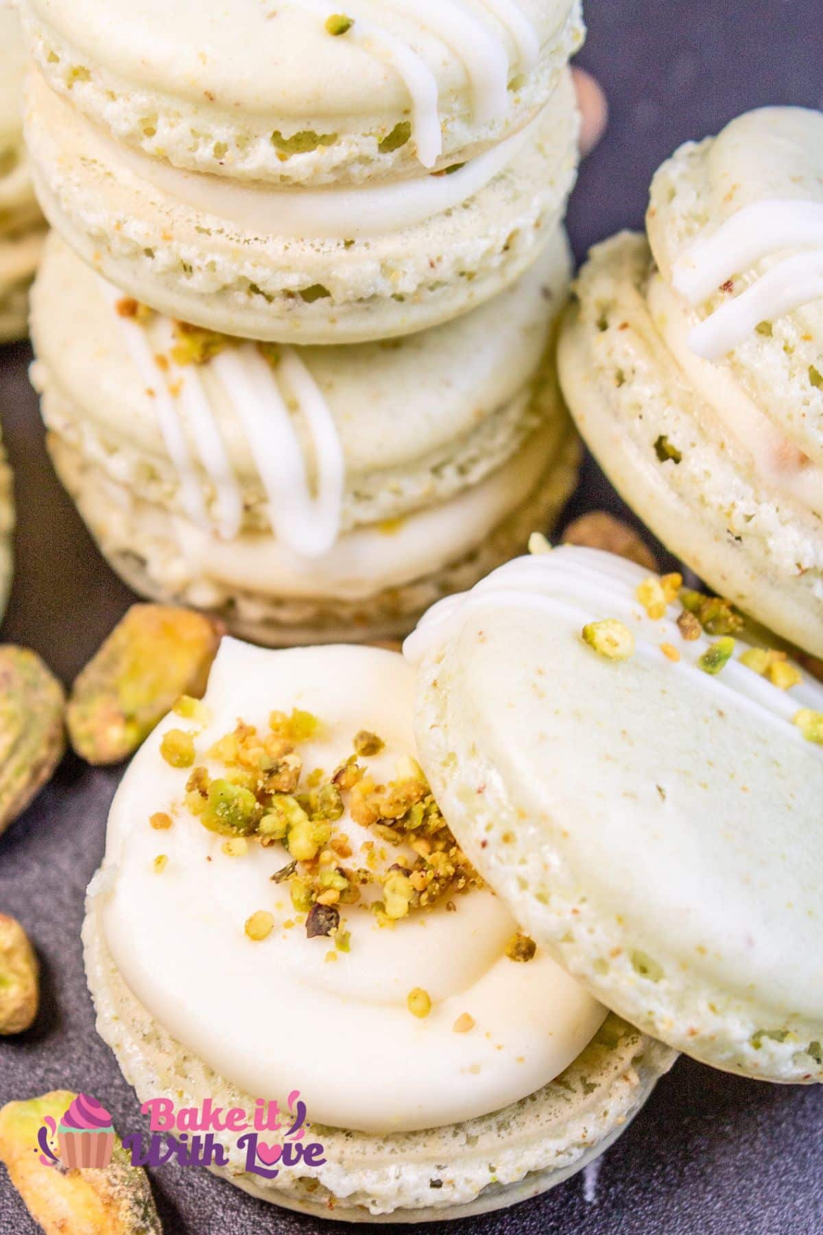 Towering stack of pistachio macarons with an open faced cookie at the base, showing the white chocolate ganache filling and sprinkled pistachio.