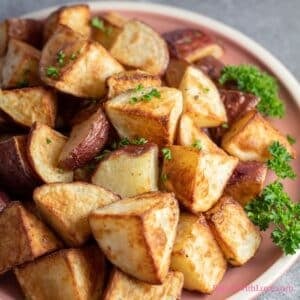 Square image of crispy roasted red potatoes on a reddish plate with parsley.