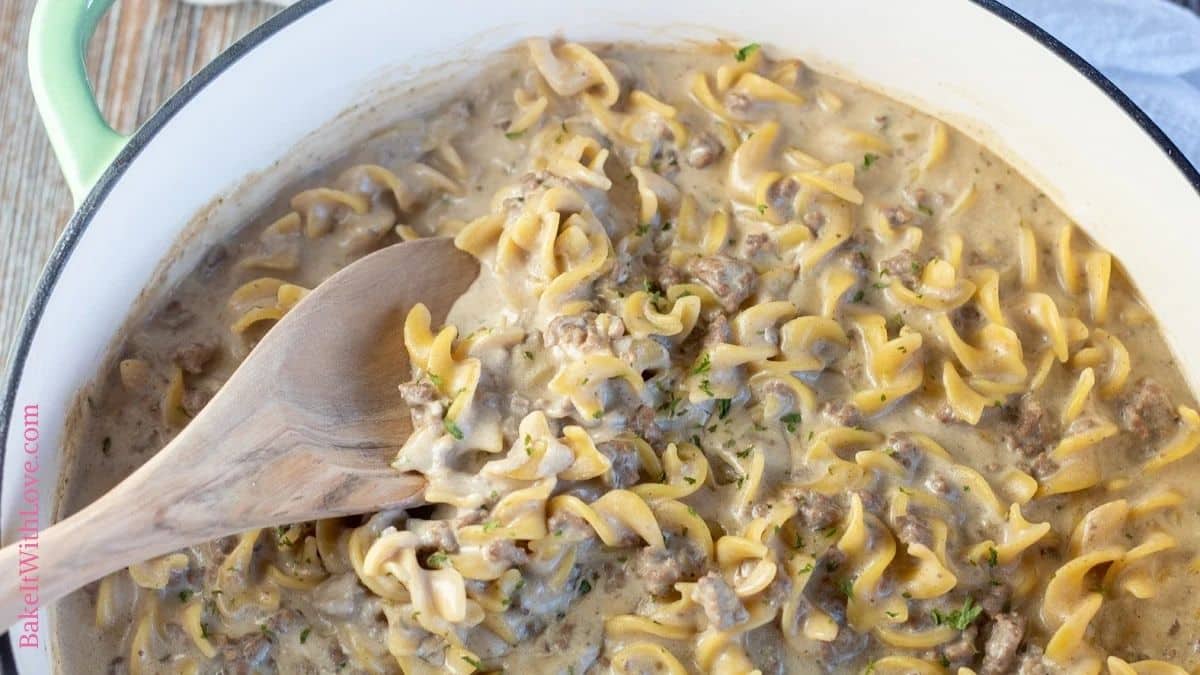 Wide image of hamburger helper beef stroganoff in a large pan with wooden spoon.