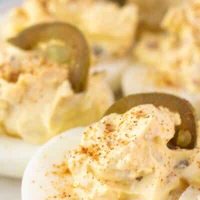 Tasty jalapeno popper deviled eggs recipe pin featuring a closeup on the plated eggs with text title.
