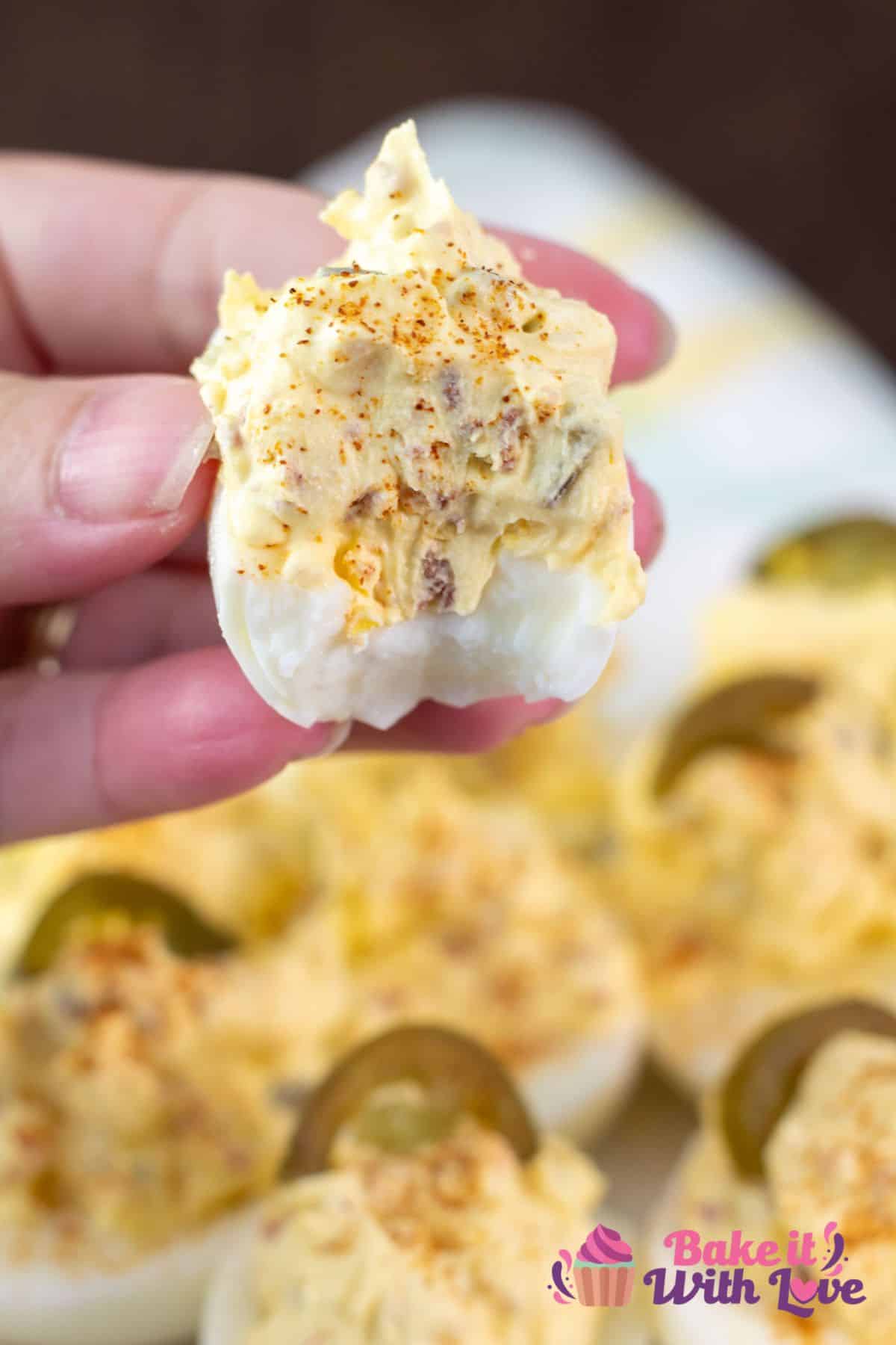 Tasty jalapeno popper deviled eggs plated with a bite out of one in my hand.