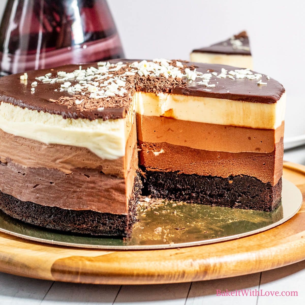 Amazing 4 layer chocolate mousse cake with a slice removed on a cake board.