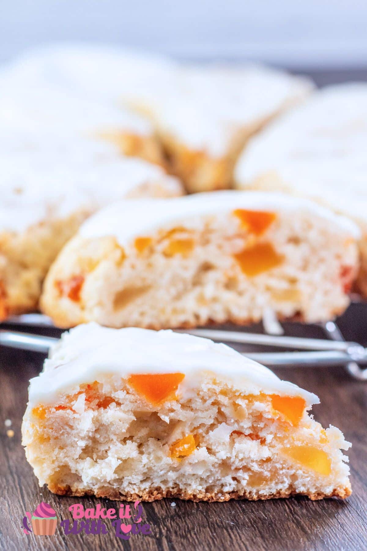 Delicious tropical fruit scones with coconut icing on a wire rack with one of the wedges cut open to show the tender crumb with colorful bits of fruit.