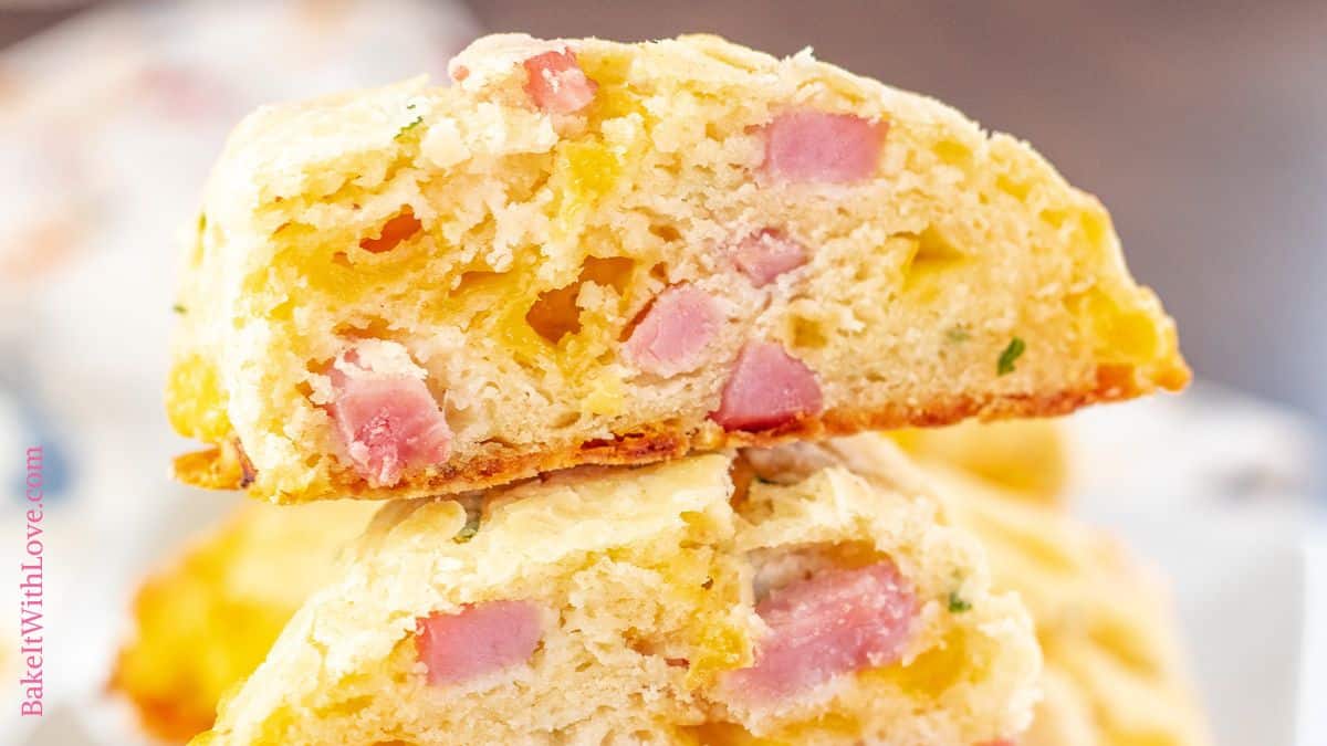 A wide image showing a close-up of two stacked scones that are perfectly golden and studded with diced ham and chives.