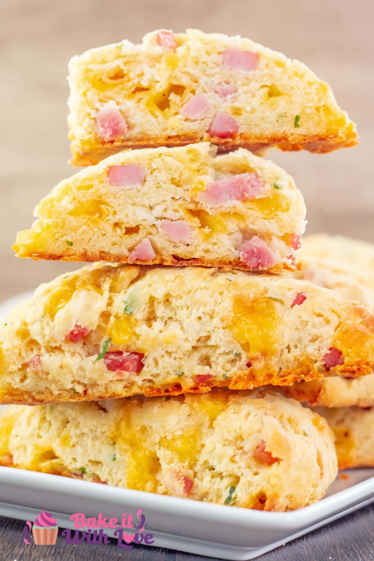 Tall image of stacked ham cheddar cheese and fresh chives scones on a serving platter with the top scone sliced in half and both open sides showing the delicate crumb.