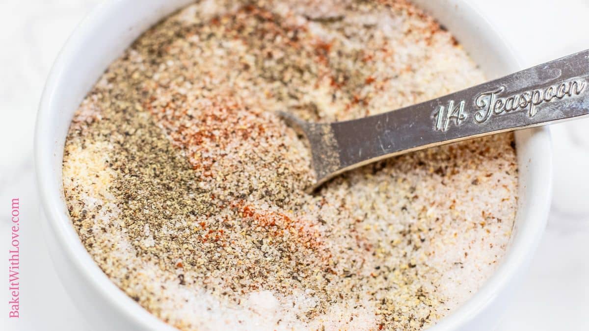 Wide closeup image of the seasoned salt after a quick stir in the white bowl, the silver teaspoon rested on the right hand side.