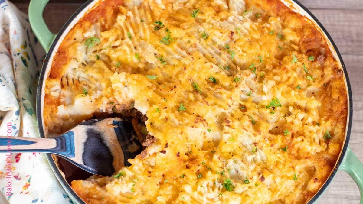 A horizontal image of a golden baked hamburger pie casserole topped with cheesy mashed potatoes with a spoon scooping out a serving.