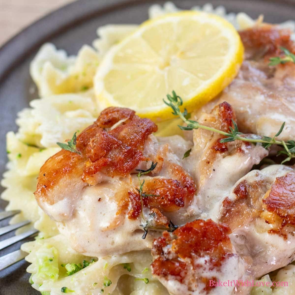 Square close up image showing plated lemon & thyme chicken thighs over bow-tie pasta.