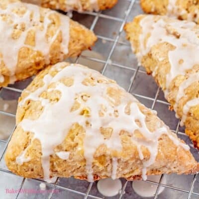 The best cinnamon apple scones recipe with freshly baked scones on a wire cooling rack allowing the drizzled icing to drip off onto a rimmed baking sheet.